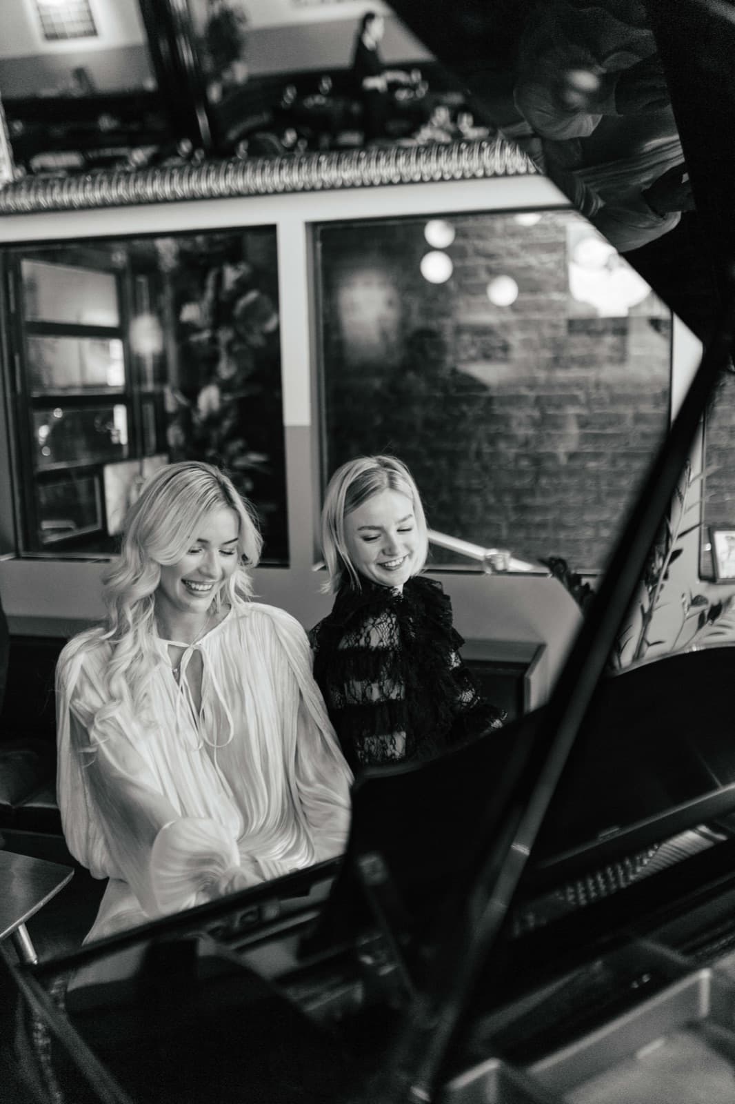 Two smiling guests reflected in a grand piano at an Edna social event